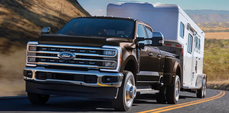 A brown 2025 Ford Super Duty towing a horse trailer down the road.