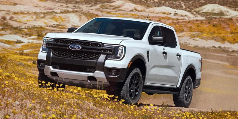 A white 2025 Ford Ranger parked in a grass field with yellow flowers