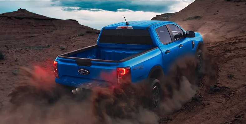 A blue 2025 Ford Ranger off-roading up a dirt hill.