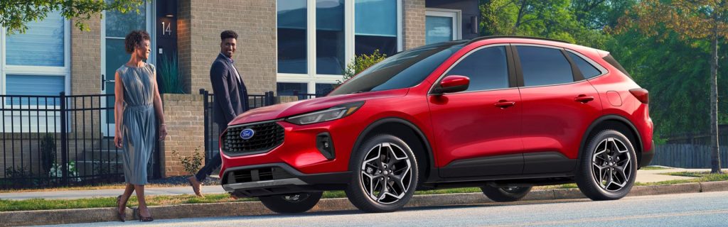 A red Ford Escape SUV parked on a residential street with two people walking nearby.